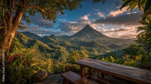 A breathtaking landscape featuring a towering mountain bathed in sunset light. Tables in the foreground invite relaxation amidst lush greenery and dramatic skies