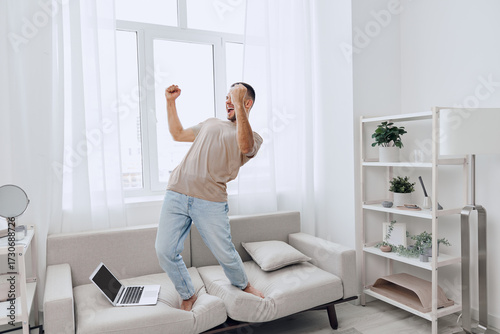 Billede på lærred Energetic man celebrating a moment of victory at home, blending personal and work life while enjoying a break from technology
