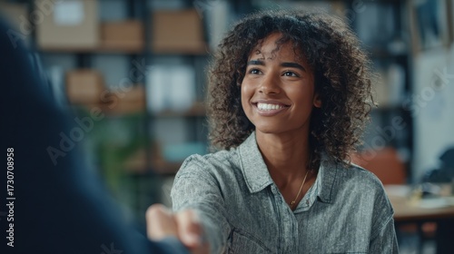 a student athletes focused expression while shaking hands with a compliance officer after signing a nil contract with office shelves softly blurred a smiling woman with curly shaking hands with a pe