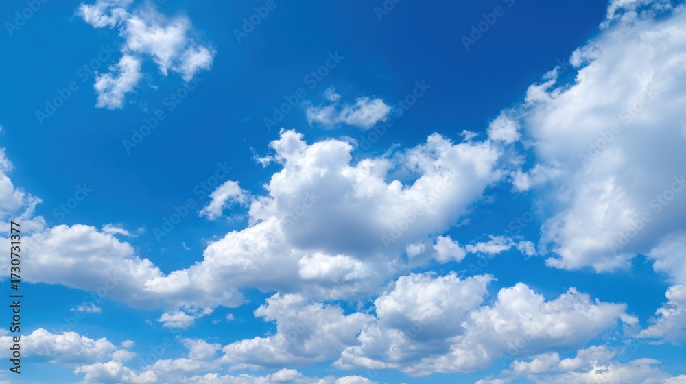 Naklejka premium A clear blue sky is dotted with large fluffy white clouds. The scene captures the beauty of a sunny day perfect for outdoor activities and enjoying nature.