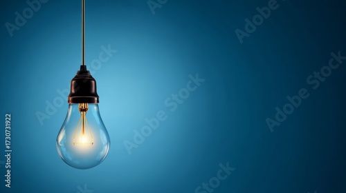A single glowing light bulb hangs from a cord against a solid blue background,