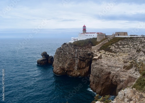  Cabo de São Vicente near Sagres, Algarve — the historic lighthouse perched on dramatic limestone cliffs overlooking the Atlantic Ocean. Golden-hour shot showing waves crashing into sea stacks and the