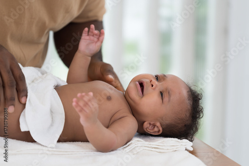 African American father wearing newborn baby diaper on white towel after taking shower. Father changing newborn baby diaper at home