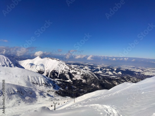 Fototapeta Naklejka Na Ścianę i Meble -  A vast snow-covered panorama from Kasprowy Wierch in Poland, featuring rugged white mountain peaks against a brilliant deep blue winter sky.
