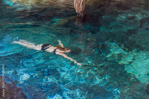 Female tourist enjoying a refreshing swim in a Mexican cenote with turquoise water. Adventure, travel, and nature exploration concept