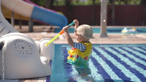 A happy little boy is enjoying himself in the pool. He is playing with a water gun and shooting at his younger brother.
