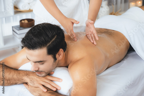 Caucasian man customer enjoying relaxing anti-stress spa massage and pampering with beauty skin recreation leisure in day light ambient salon spa at luxury resort or hotel. Quiescent