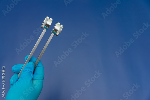 Quadro su tela Blue Gloved Hands Holding tuning fork On blue Background, medical instruments in