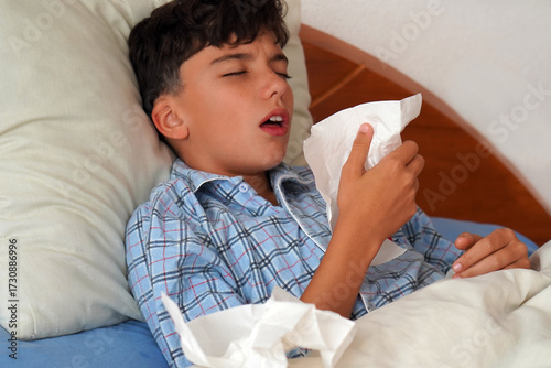 child in pajamas sick in bed with a cough and a tissue