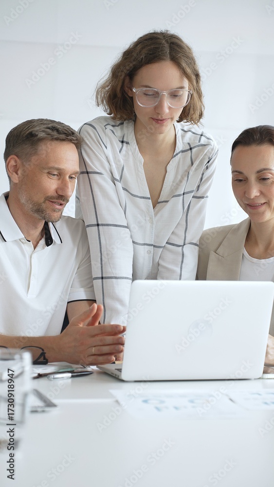 Obraz premium Professional team reviewing project data on laptop, working together in modern office environment, collaborating with focused corporate energy