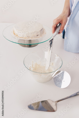 Young woman with slim hands decorates a chocolate sponge cake with a palette knife and butter cream on a special stand to assemble a delicious cake. Homemade chocolate sponge cake.