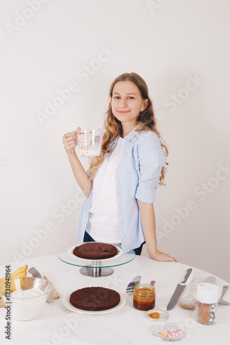A beautiful young woman with long hair filling a chocolate sponge cake with milk on a special stand. Home made chocolate sponge cake, traditional cooking, young housewife.