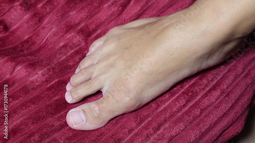 Horizontal 4K video. Top view. White woman's leg rests on dark pink, burgundy blanket. Muscle in female foot is tensed. Concept of dream, sleep, relax, skin care, spa, lazy, rest, relaxation, wellness