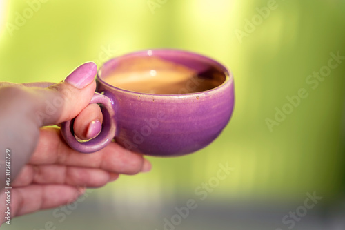Espresso coffee in a small lilac mug. woman holding a ristretto on green background