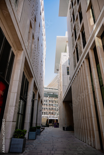 A modern architectural corridor flanked by tall beige buildings under clear blue skies, showcasing symmetry, urban texture, and depth perspective in the heart of downtown Doha.
