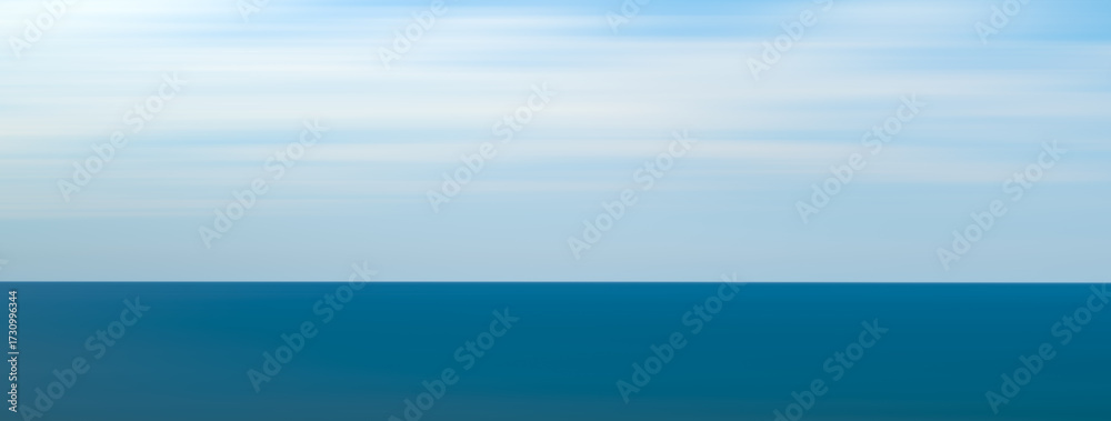 Obraz premium A wide panorama of the blue ocean against a white sky. The sky is clear and the ocean is calm.