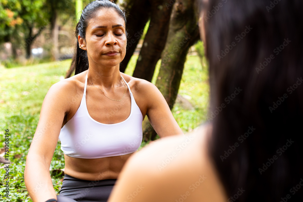 Fototapeta premium Teaching meditation, Latin woman aged 48 guides her apprentice in an outdoor yoga practice, conveying calm and inner balance in a natural environment.