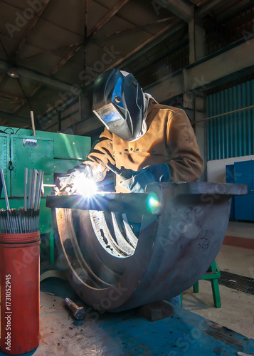 Tecnico en taller mecanico haciendo trabajos de soldador o soldadura en ua pieza metalica, usando su equipo de proteccion personal