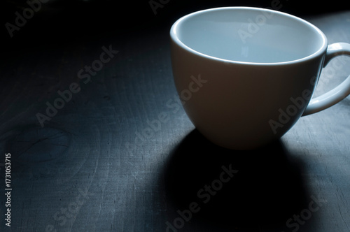 Taza blanca vacia, sobre una mesa oscura con luz tenue y a contraluz. Copy space, imagen horizontal
