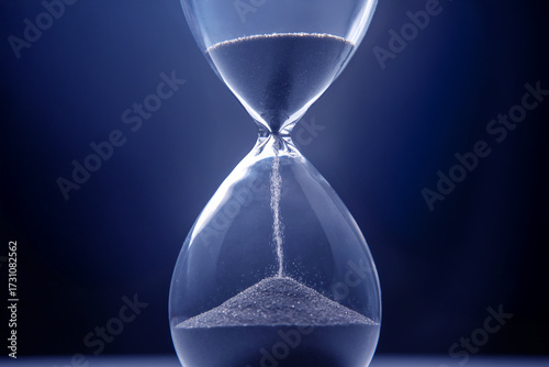Hourglass filled with dark sand against a blue background captures the essence of time passing