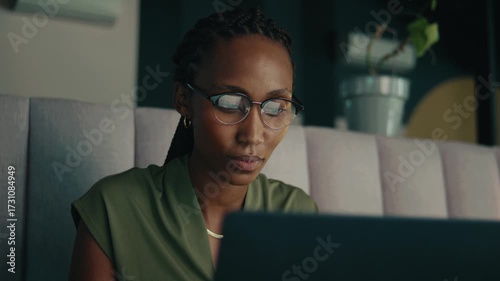 A black young businesswoman in glasses using laptop in office lounge