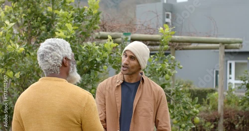 Senior African American friend telling joke to cheer South Asian friend laughing in apple orchard
