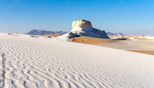 Rippled white sand dunes and chalk rock formations in the famous White Desert National Park, Egypt, under a clear blue sky.