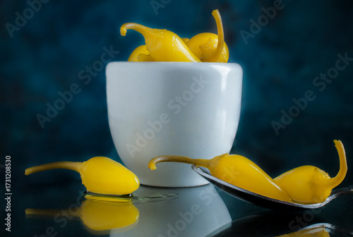 Peperoncino en una tacita blanca y sobre una cuchara sobre una superficie reflectiva en un fondo azul oscuro, imagen horizontal
