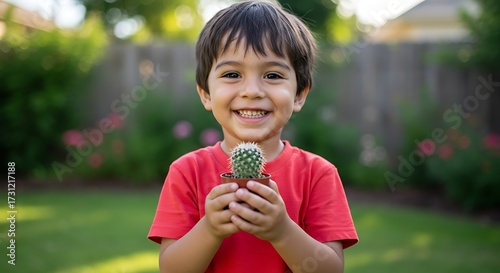 Smiling child holding small potted cactus outdoors with green background