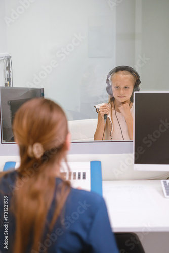 Audiometry hearing test with child and female audiologist doctor at her 40th. Pediatric ear exam in clinic. Hearing healthcare. Hearing loss prevention. Girl patient in headphones clicking button 