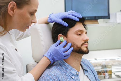 Audiologist removing custom molded ear impression for hearing aid or ear plug fitting. Clinical process for personalized hearing protection.