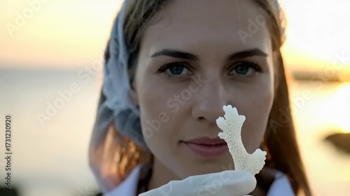 Woman holding white object near face against sunset sky