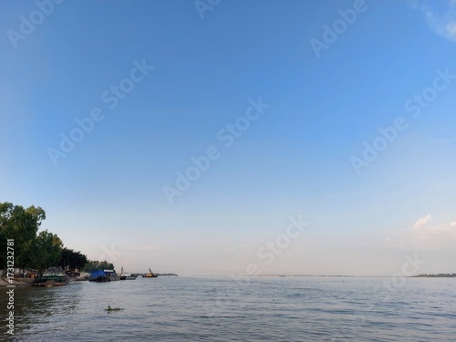 Calm water reflects a vast blue sky over a rocky shoreline