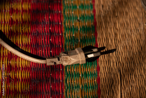 A still life of an old electrical plug on a traditional Vietnamese woven straw mat, a concept of modernity meeting tradition in daily life. 