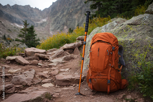 Orange hiking backpack with trekking pole on rocky trail