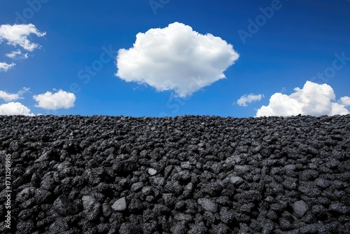 Dark, rocky pile against a vibrant blue sky with a single large white cloud