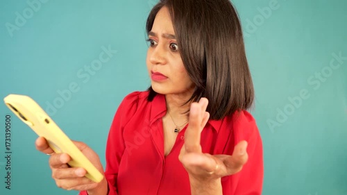 Closeup of shocked confused young Indian woman hold mobile using phone online internet connection problem error receiving bad news by sms feels worry anxiety stress, isolated over blue background.