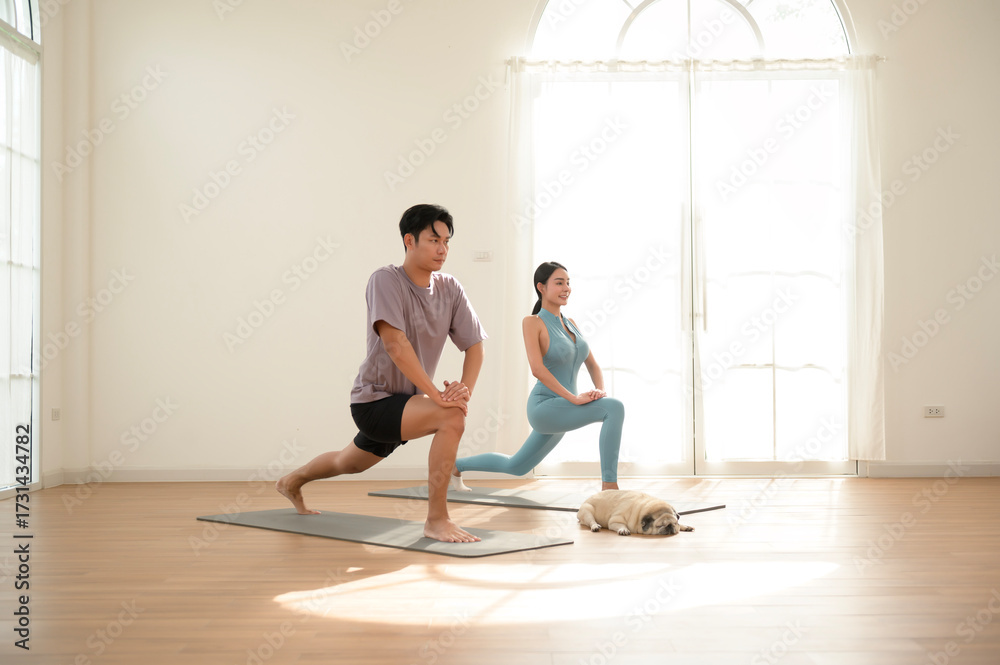 Fototapeta premium Couple Practicing Yoga at Home With a Dog Resting on the Floor in Natural Light