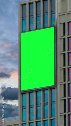 Green chroma key blank vertical billboard mock up in city center for advertising on skyscrapers with beautiful clouds background