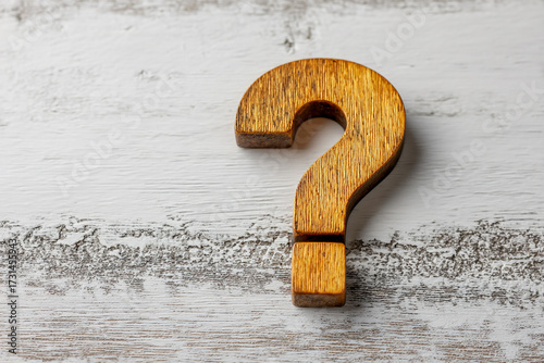 A wooden question mark symbol rests on a rustic white textured surface