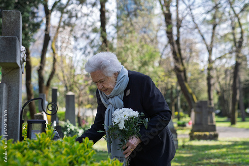 Quadro su tela Elderly widow bringing flowers to a grave at cemetery.