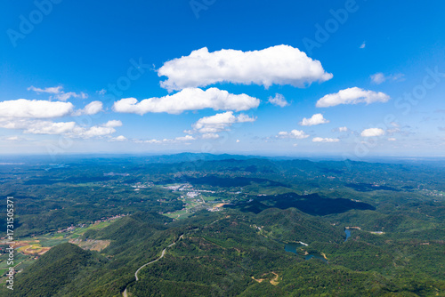 Dahong Mountain, Suizhou China, shows rolling green hills under a bright blue sky with fluffy white clouds.