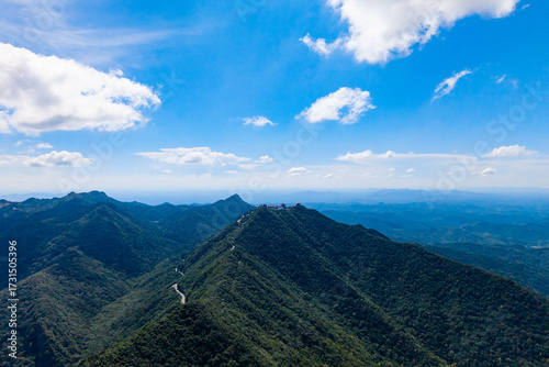 Dahong Mountain rises under a blue sky with clouds, presenting vast green valleys and a winding path reaching toward the distant horizon.
