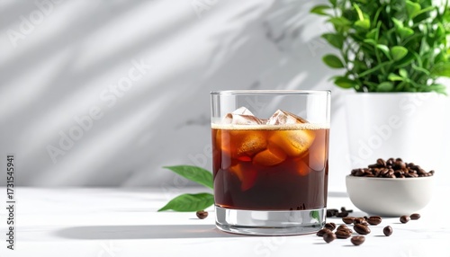 Refreshing cold brew coffee is displayed in a clear glass with ice cubes, surrounded by coffee beans, a decorative green plant, and natural light creating shadows, showcasing a simple and elegant...