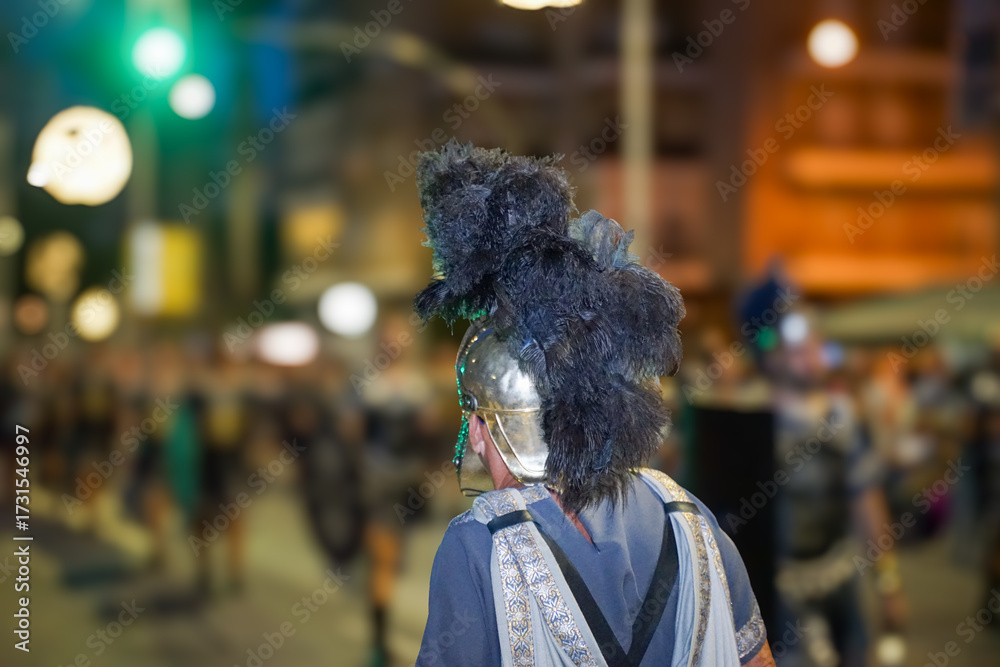 Obraz premium A person from behind, wearing a Roman helmet, parading through the streets of Cartagena on its main day of festivities