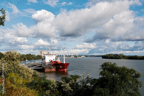 Large cargo ship docked at industrial port with cranes under dramatic cloudy sky