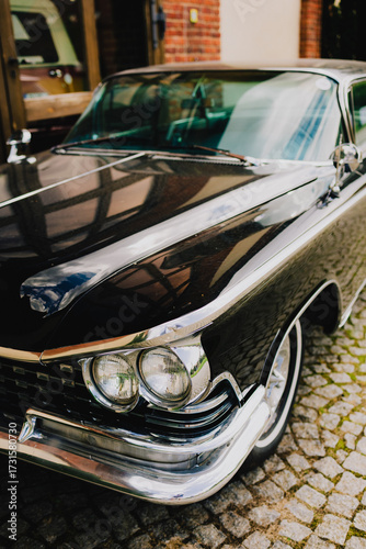 Classic black car reflecting surrounding buildings while parked on cobblestone street, highlighting polished chrome details and exuding vintage charm and elegance. Vintage black car parked on street