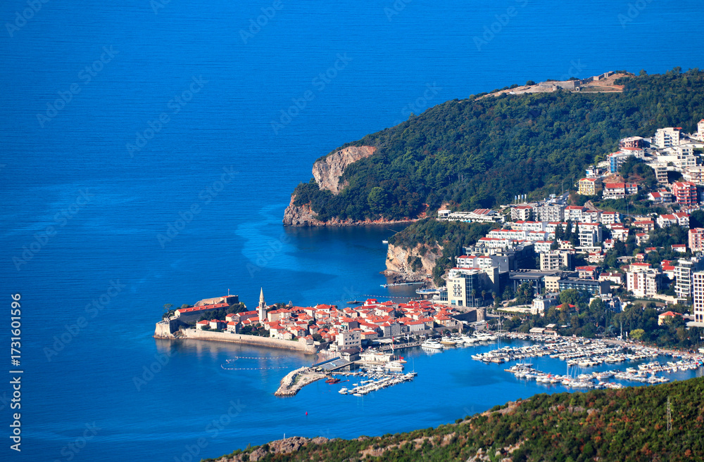 Naklejka premium Aerial view of picturesque scenery - old town and Adriatic sea, Budva, Montenegro. Bird's-eye view of beautiful scene with medieval houses and seascape. Topic of summer vacation, travel, cruise, tour