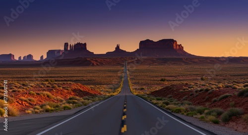 Open road leading to distant mesas at sunset with dramatic orange and purple skies and copy space
