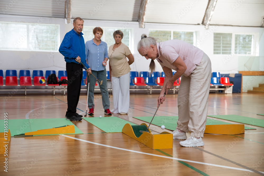 Obraz premium elderly group plays mini golf for competitions in the sprot hall. Kidult gaming in the gym. Active retirement community. dopamine hobbies. an active and healthy lifestyle in retirement. 